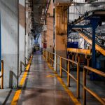 Vista ampla do interior de uma fábrica moderna, com máquinas industriais e sistemas de esteiras.