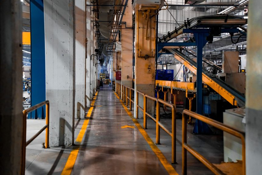 Vista ampla do interior de uma fábrica moderna, com máquinas industriais e sistemas de esteiras.