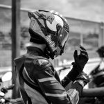 Motociclista vestido com equipamento de corrida ajusta o capacete ao ar livre.