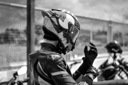 Motociclista vestido com equipamento de corrida ajusta o capacete ao ar livre.