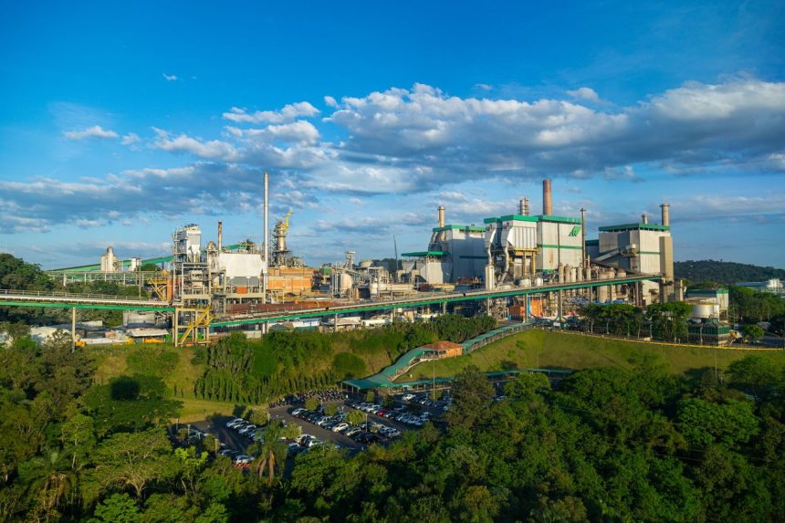 Vista aérea de uma grande fábrica cercada por vegetação densa.