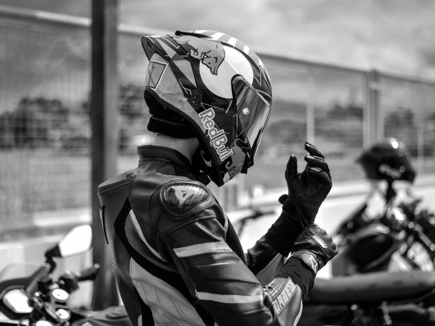 Motociclista vestido com equipamento de corrida ajusta o capacete ao ar livre.